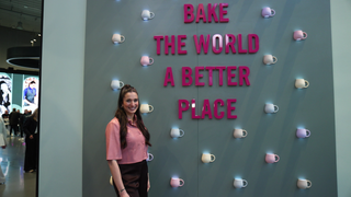 Sally Özcan steht vor einer Wand auf der „Bake the world a better place“ steht.