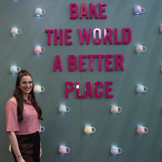 Sally Özcan steht vor einer Wand auf der „Bake the world a better place“ steht.