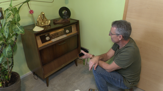 Peter Keßner kniet vor einer alten Musiktruhe.