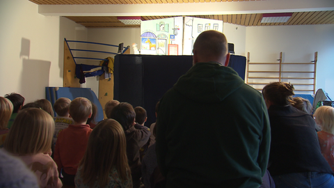 Viele Kinder schauen auf eine Bühne mit einem Kasperletheater.