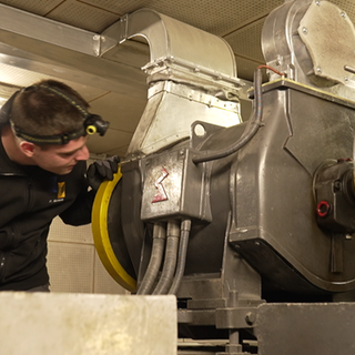 Ein Mann mit Stirnlampe arbeitet an einem alten Aufzug.