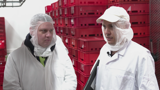 Zwei Männer in weißen Schutzanzügen stehen vor vielen roten Kisten.