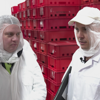 Zwei Männer in weißen Schutzanzügen stehen vor vielen roten Kisten.