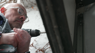 Christian Bauerle steht an einem Garagentor und bohrt mit einem Akkubohrer ein Loch hinein. 