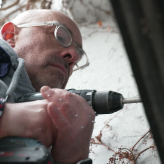 Christian Bauerle steht an einem Garagentor und bohrt mit einem Akkubohrer ein Loch hinein. 