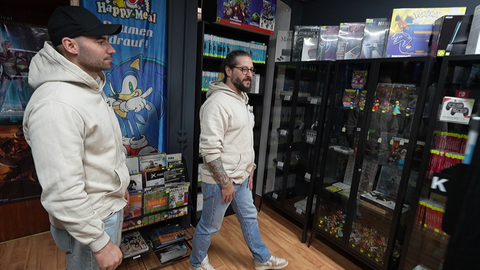 Zwei Männer laufen durch einen Laden. Überall im Hintergrund sind Retro-Spiele und Retro-Konsolen. 