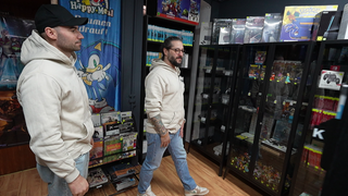 Zwei Männer laufen durch einen Laden. Überall im Hintergrund sind Retro-Spiele und Retro-Konsolen. 