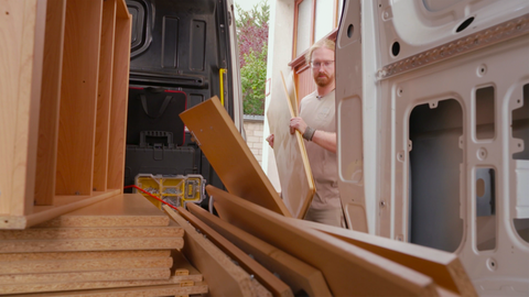 Ein junger Mann trägt einen auseinandergebauten Schrank in einen Transporter. 