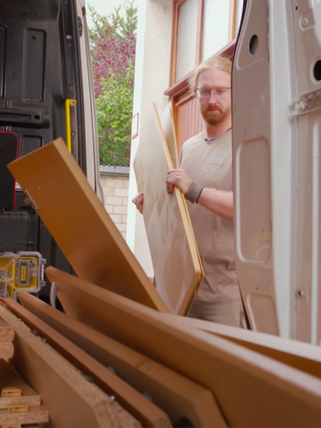 Ein junger Mann trägt einen auseinandergebauten Schrank in einen Transporter. 