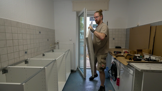 Ein Mann trägt eine Arbeitsplatte in einen Raum, in dem eine Küche aufgebaut wird. 