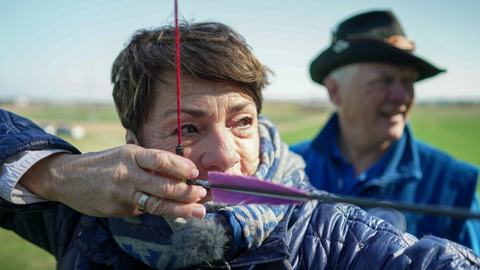 Sonja Faber-Schrecklein hat einen Bogen zum Schießen gespannt. Sie guckt konzentriert in die Ferne. 