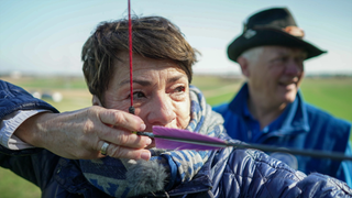 Sonja Faber-Schrecklein hat einen Bogen zum Schießen gespannt. Sie guckt konzentriert in die Ferne. 