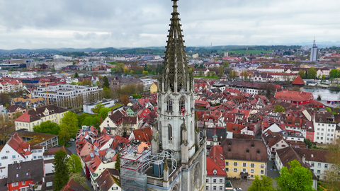 Das Münster in Konstanz aus der Vogelperspektive. Ein Mann in roter Arbeitskleidung klettert daran hoch.