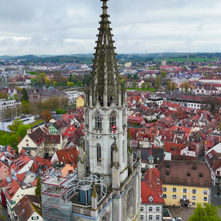 Das Münster in Konstanz aus der Vogelperspektive. Ein Mann in roter Arbeitskleidung klettert daran hoch.