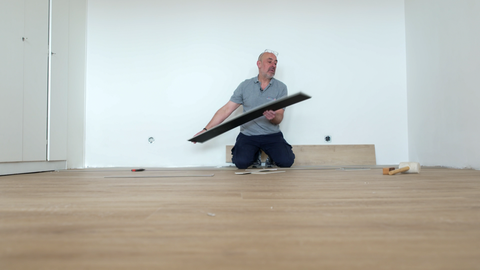 Ein Mann kniet in einem leeren Raum. Er verlegt Laminat.