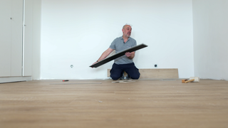 Ein Mann kniet in einem leeren Raum. Er verlegt Laminat.