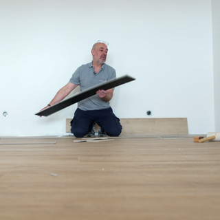 Ein Mann kniet in einem leeren Raum. Er verlegt Laminat.