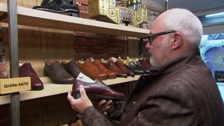 Ein Kunde steht in einem Second Hand-Schugeschäft und schatet sich verschiedene Lederschuhe an.