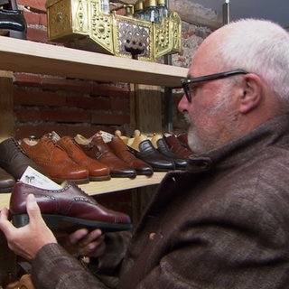 Ein Kunde steht in einem Second Hand-Schugeschäft und schatet sich verschiedene Lederschuhe an.