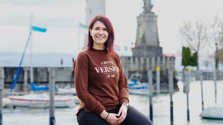 Aline Manglus sitzt vor dem Lindauer Leuchtturm und lächelt in die Kamera.