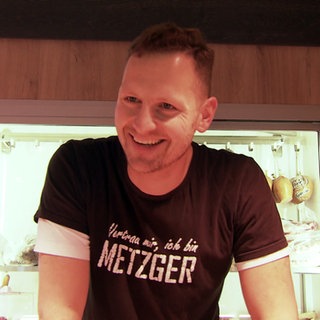 Philipp Burkhardt steht in seinem Marktwagen und trägt ein schwarzes T-Shirt. Er lächelt. Im Hintergrund hängen Würste.