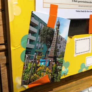 Ein Foto einer Nachbildung des Eiffelturms hängt an einem gelben Poster. Es ist mit orangenem Klebeband befestigt.