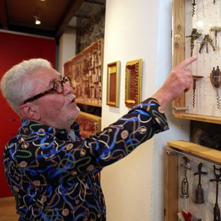 Bernhard Maurer trägt ein buntes Hemd zeigt mit dem rechten Arm auf eine Sammlung von verschiedenen Korkenziehern in seinem Museum in Burkheim.