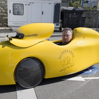 Albrecht Maurer sitzt in seinem knallgelben Velomobil und steht damit auf einer Fahrradstraße. Es ist nur Albrechts Kopf zu sehen, der aus dem Velomobil heraus schaut.