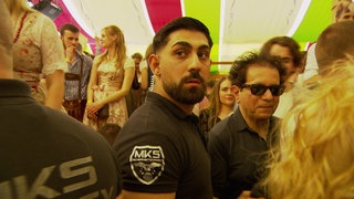 Ein Mitarbeiter der Security steht in einem Bierzelt auf dem Cannstatter Frühlingsfest. Er ist von einer Menschenmenge umgeben.