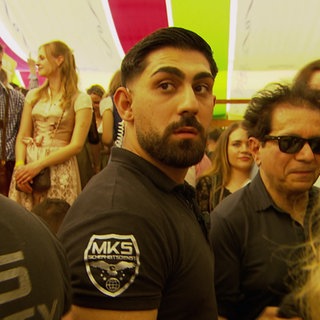 Ein Mitarbeiter der Security steht in einem Bierzelt auf dem Cannstatter Frühlingsfest. Er ist von einer Menschenmenge umgeben.