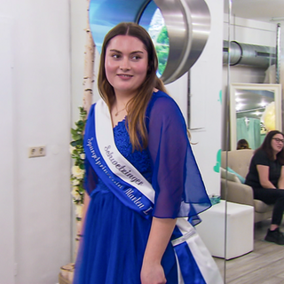 Marlen trägt ein blaues Kleid und eine Schärpe mit der Aufschrift „Schwetzinger Spargelprinzessin Marlen I.“.
