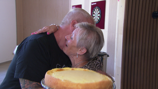 Erzieherin Gisela umarmt ein ehemaliges Kind, das sie betreut hat. In der anderen Hand hält sie einen Kuchen.