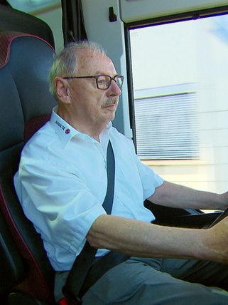 Georg Nußbaum trägt ein weißes Hemd und sitzt am Lenkrad eines Reisebusses. Er schaut nach rechts.