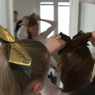 Eine Tochter hilft ihrer Mutter mit deren Cheerleader-Outfit