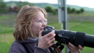 Birding - junge Frau mit Fotokamera in der Hand beim Beobachten von Vögeln