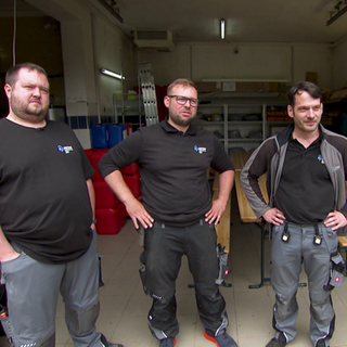 Drei Techniker stehen vor einer kleiner Lagerhalle