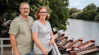 Ulrike und Christoph Brandner stehen auf einem Balkon. Beide lächeln in die Kamera. 