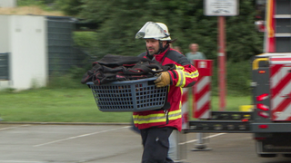 Ein Feuerwehrmann in Ausrüstung trägt einen Korb mit Feuerwehrausrüstung. 