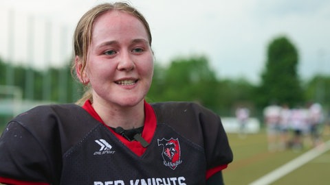 American Football-Spielerin Sophie Hausch steht auf einem Sportplatz und trägt eine schwarze Football-Uniform. Ihr Gesischt ist rot und leicht verschwitzt vom Training.