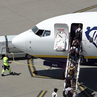 Ein Flugzeug steht auf dem Rollfeld des Flughafens Baden-BadenKarlsruhe. Passagiere steigen ein, links hinter dem Flugzeug sieht man den Kofferwagen.