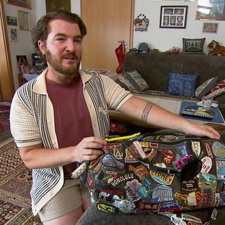 Weltenbummler Marcus O'Shea mit seiner Reisetasche, die Aufnäher von vielen Reisezielen hat.