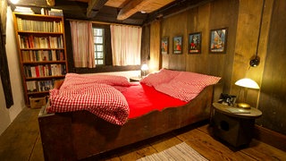 Ein Schlafzimmer in einem Bauernhaus. Die Wände, der Boden und die Decke sind aus Holz. 