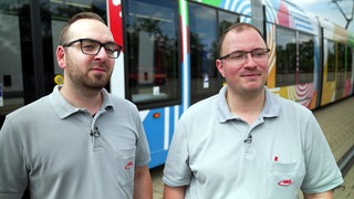 Marco und Daniel Rungenhagen stehen in Freiburg vor einer Straßenbahn