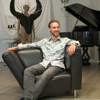 Der 22-jährige Julian Prohaska sitzt auf einem Sessel in seinem Atelier. Hinter ihm eine Schaufensterpuppe und ein Flügel.
