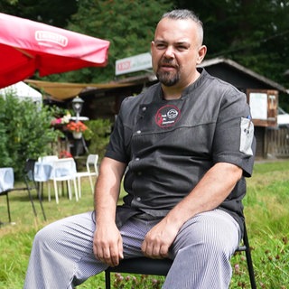 Kioskbesitzer Daniel Müller sitzt auf einem Stuhl vor seinem Kiosk