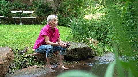 Frau sitzt mit Füßen in einem Bach