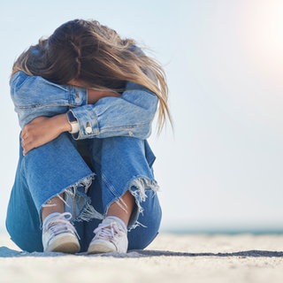 Frau kauert in der Sonne am Sandstrand auf dem Boden