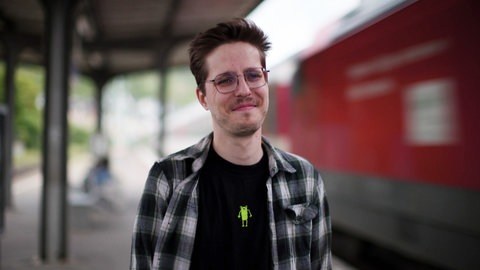 Mann steh einem Bahnhofgleis neben einem einfahrenden Zug.