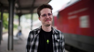 Mann steh einem Bahnhofgleis neben einem einfahrenden Zug.