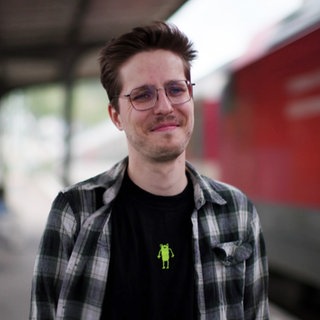 Mann steh einem Bahnhofgleis neben einem einfahrenden Zug.